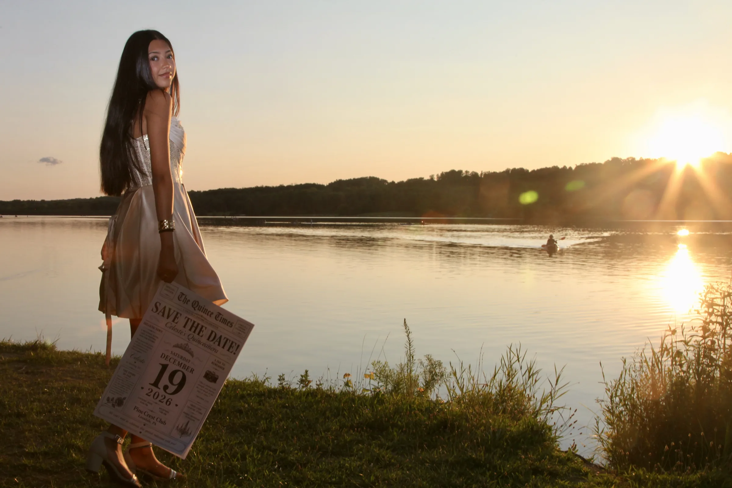 Celeste by the lake at sunset, holding the Save the Date newspaper.